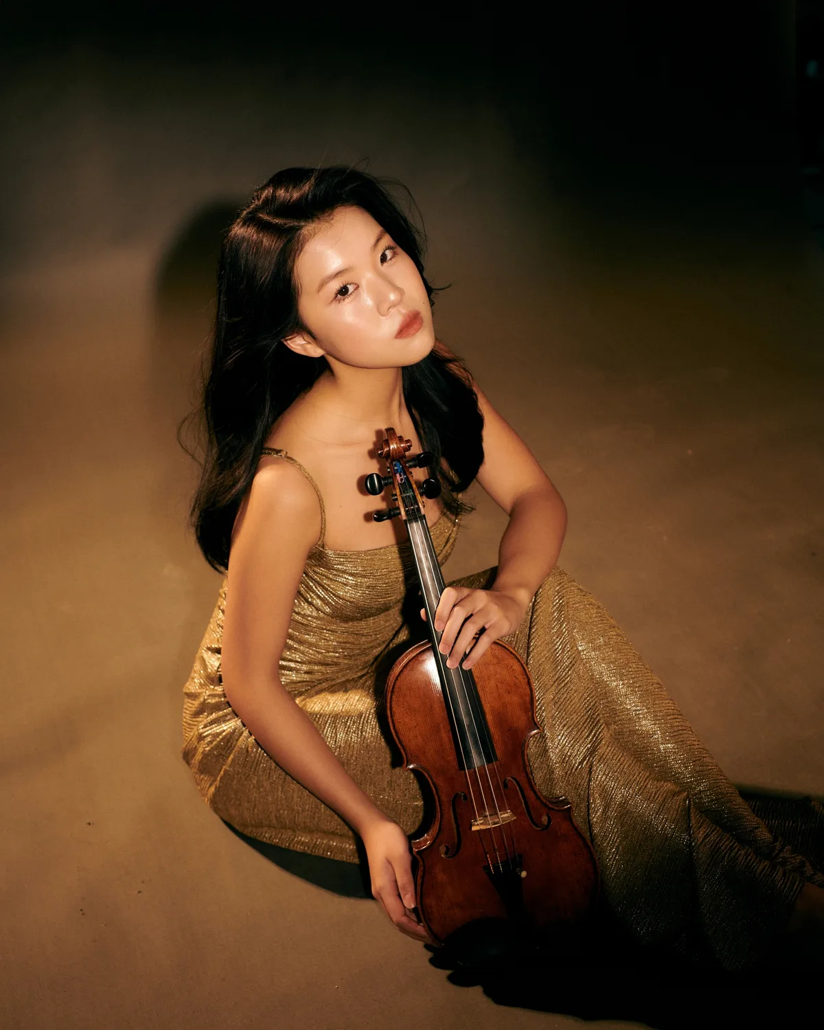 Obwohl Klara Cheng 2023 erst 15 Jahre alt war, wurde sie wegen ihres Talents an die Zürcher Hochschule der Künste aufgenommen. Eine Geigerin sitzt in einem goldenen Kleid am Boden.